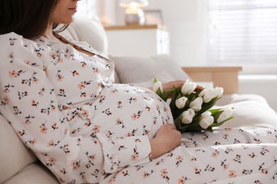 Young pregnant woman with flowers at home, closeup