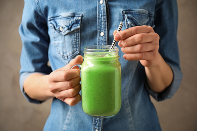 Woman holding tasty kale smoothie on brown background, closeup