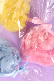 Photo of Packaged sweet cotton candies on violet background, flat lay