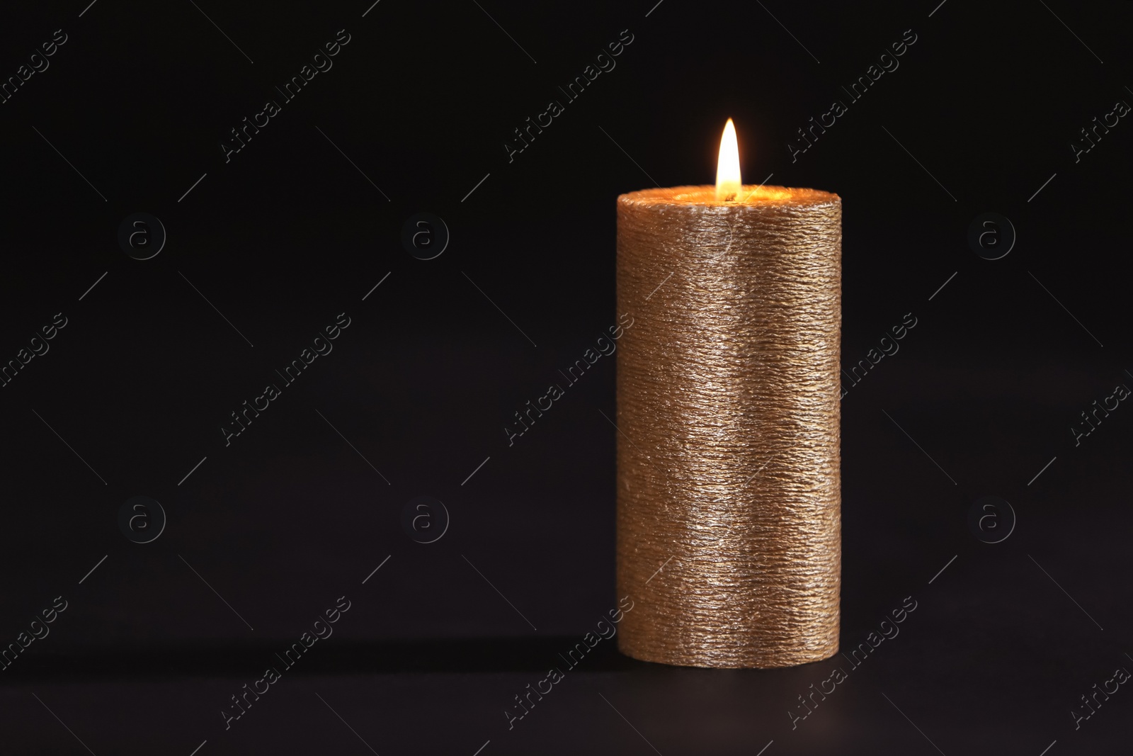 Photo of Burning gold candle on black background, space for text