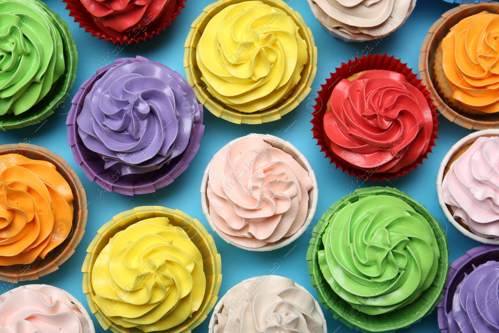 Photo of Many tasty cupcakes with bright cream on light blue background, flat lay