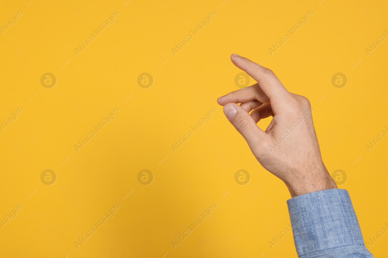 Photo of Man holding something against yellow background, closeup on hand. Space for text