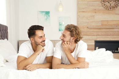 Photo of Happy gay couple lying on bed at home