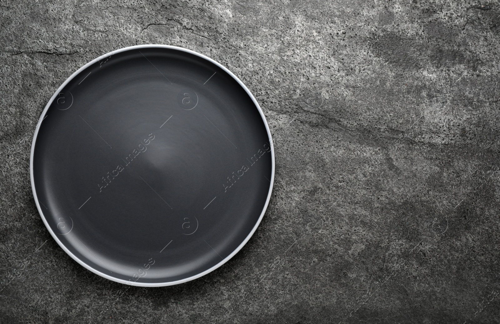 Photo of New dark plate on grey table, top view. Space for text