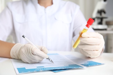 Photo of Doctor holding test tube with urine sample for analysis at table in laboratory, closeup