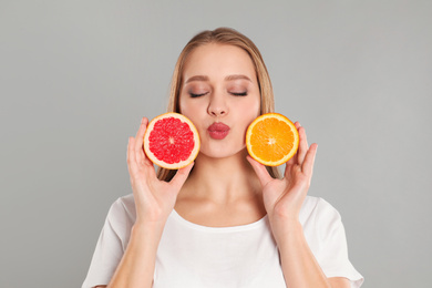 Photo of Young woman with cut orange and grapefruit on grey background. Vitamin rich food