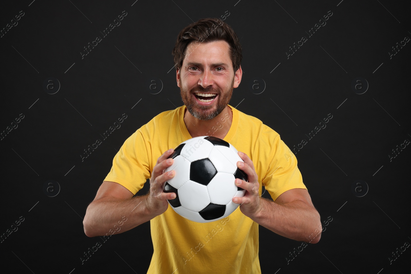 Photo of Emotional sports fan with soccer ball on black background