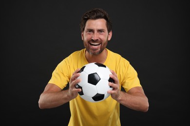 Photo of Emotional sports fan with soccer ball on black background