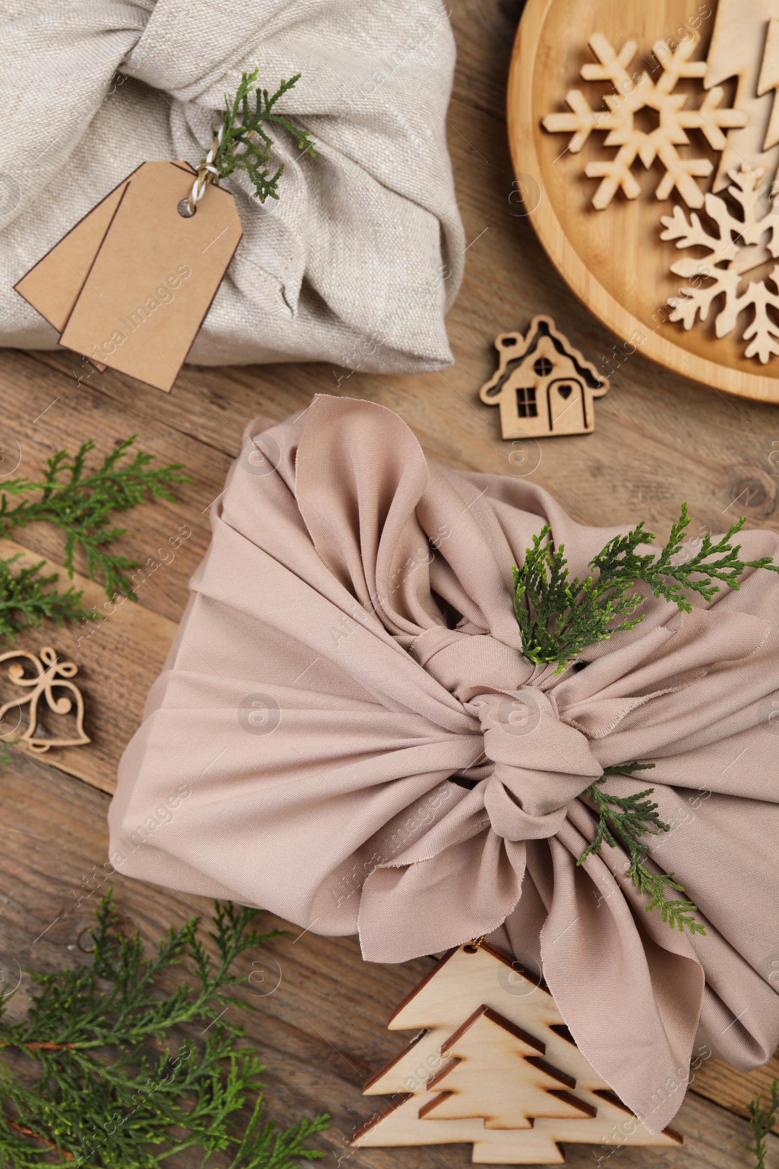 Photo of Furoshiki technique. Gift packed in fabric, thuja branches and festive decoration on wooden table, flat lay