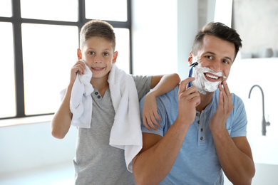 Son wiping face with towel while his dad shaving in bathroom