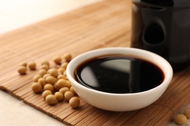 Photo of Soy sauce in bowl and soybeans on bamboo mat, closeup