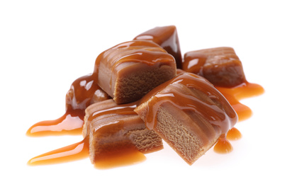 Photo of Pieces of caramel with sauce isolated on white