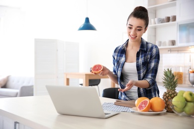 Young blogger with fruits and laptop on kitchen
