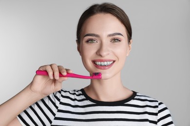 Photo of Young woman brushing teeth with charcoal toothpaste on grey background