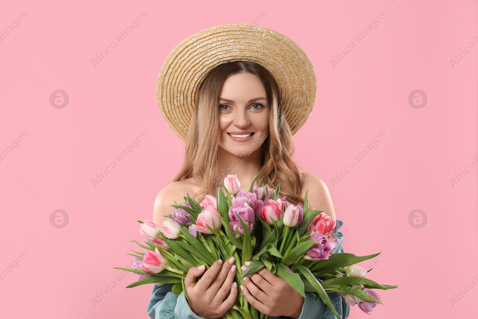 Photo of Happy young woman in straw hat holding bouquet of beautiful tulips on pink background