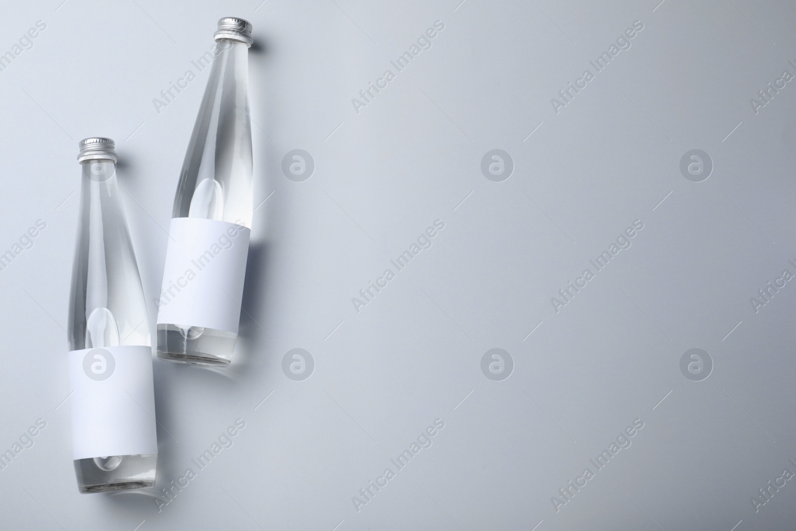 Photo of Glass bottles with soda water on light background, flat lay. Space for text