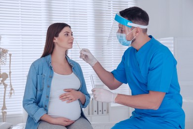 Doctor taking nasal smear of pregnant woman for coronavirus test in clinic