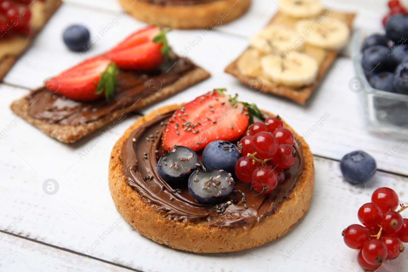 Photo of Fresh rye crispbreads and rusks with different toppings on white wooden table, closeup