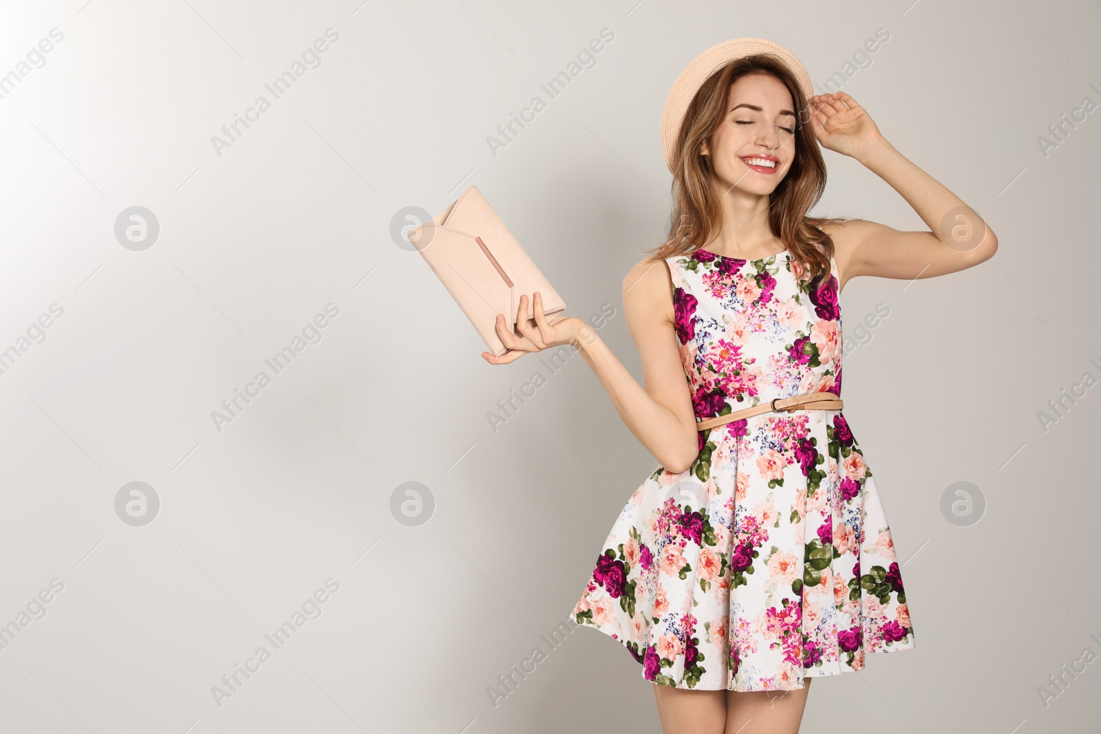 Photo of Young woman wearing floral print dress with clutch purse on light background. Space for text