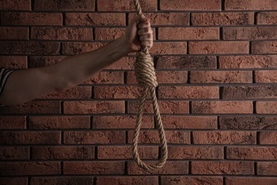 Photo of Man holding rope noose near brick wall, closeup