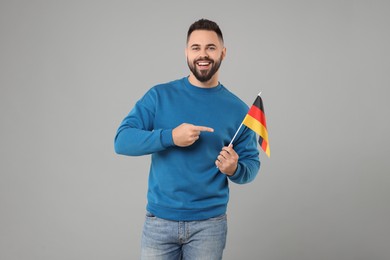 Young man holding flag of Germany on light grey background