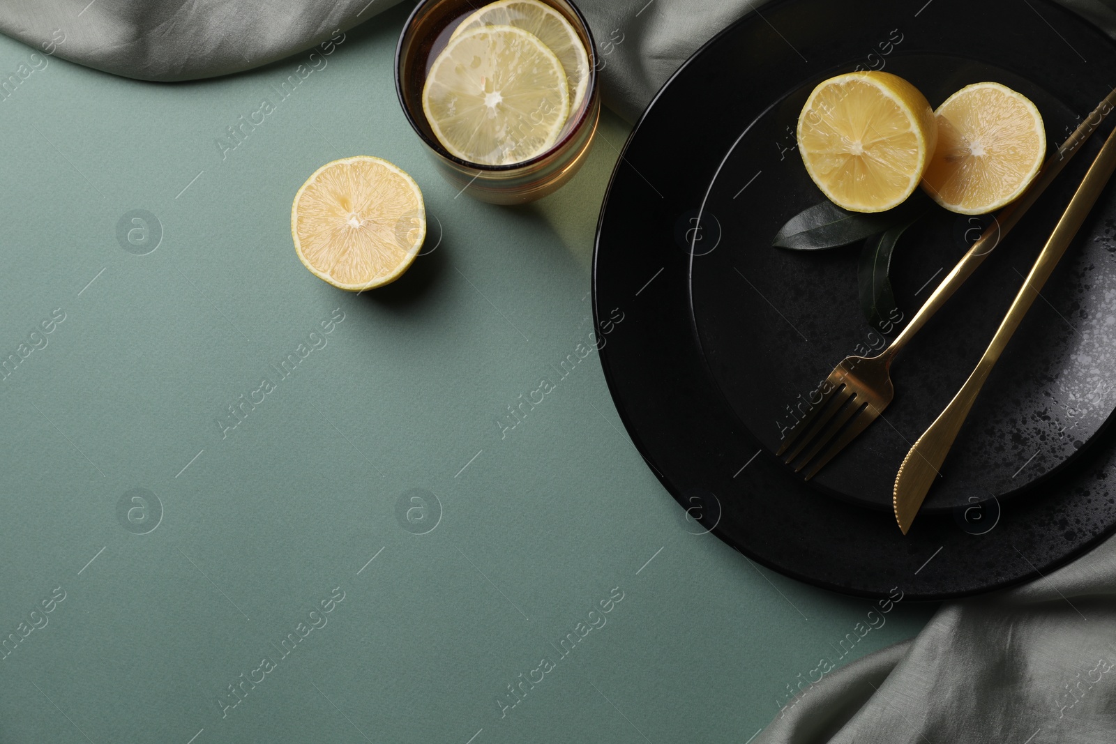 Photo of Stylish table setting. Plates, cutlery and tea with lemon on olive background, top view. Space for text