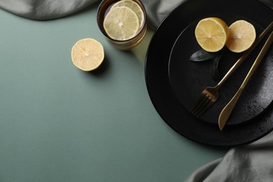 Stylish table setting. Plates, cutlery and tea with lemon on olive background, top view. Space for text