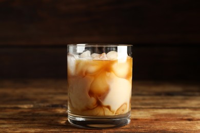 Photo of Glass of coffee with milk and ice cubes on wooden table