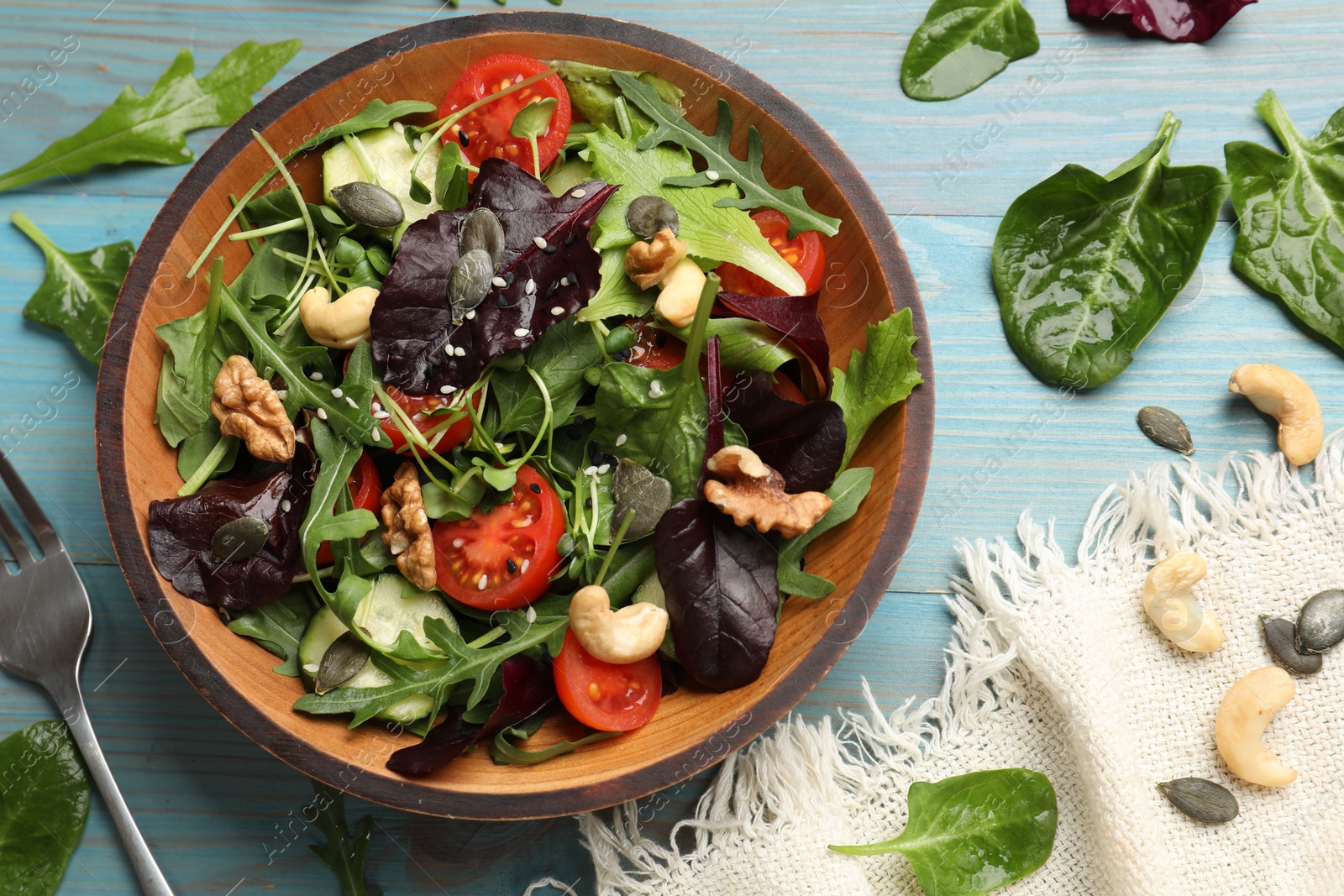 Photo of Tasty fresh vegetarian salad and fork on light blue wooden table, top view