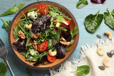 Tasty fresh vegetarian salad and fork on light blue wooden table, top view