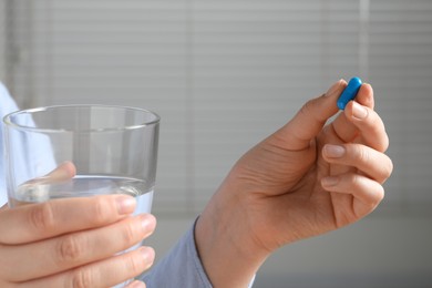 Woman with pill and glass of water on blurred background, closeup