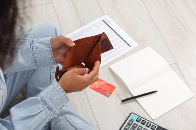 Photo of Woman with empty wallet and credit card planning budget on floor, closeup. Debt problem