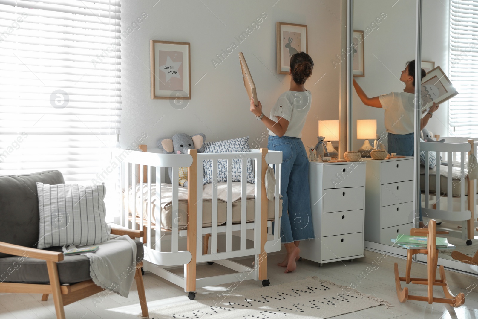 Photo of Decorator hanging pictures on wall in baby room. Interior design