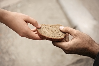 Photo of Woman giving poor homeless person pieces of bread outdoors, closeup