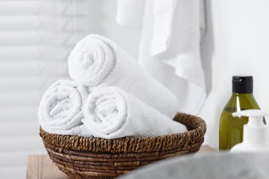 Photo of Wicker bowl with rolled bath towels on wooden table indoors