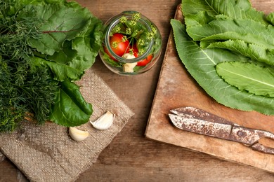 Photo of Fresh green herbs, jar with tomatoes, garlic and scissors on wooden table, flat lay