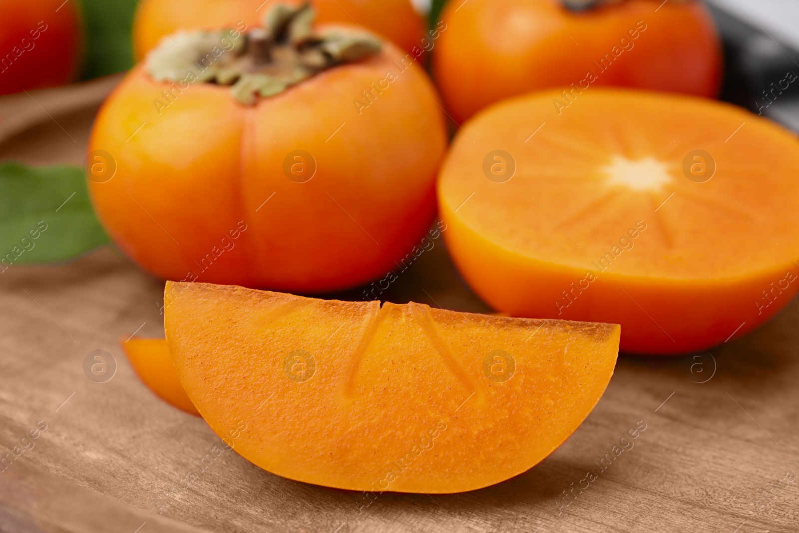 Photo of Whole and cut delicious ripe persimmons on wooden table, closeup