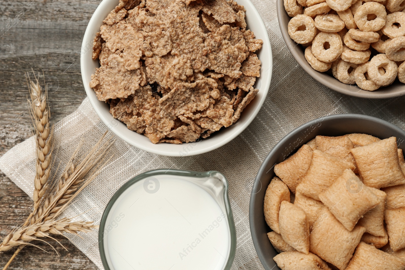 Photo of Different breakfast cereals, milk and spikelets on wooden table, flat lay