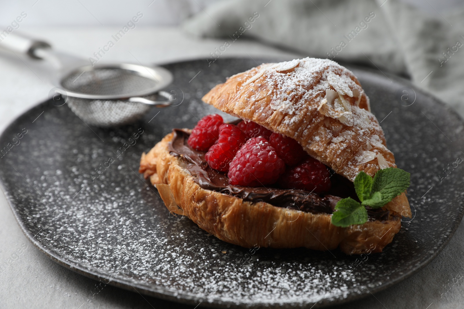 Photo of Delicious croissant with raspberries, chocolate and powdered sugar on table, closeup