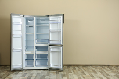 Modern refrigerator near beige wall, space for text