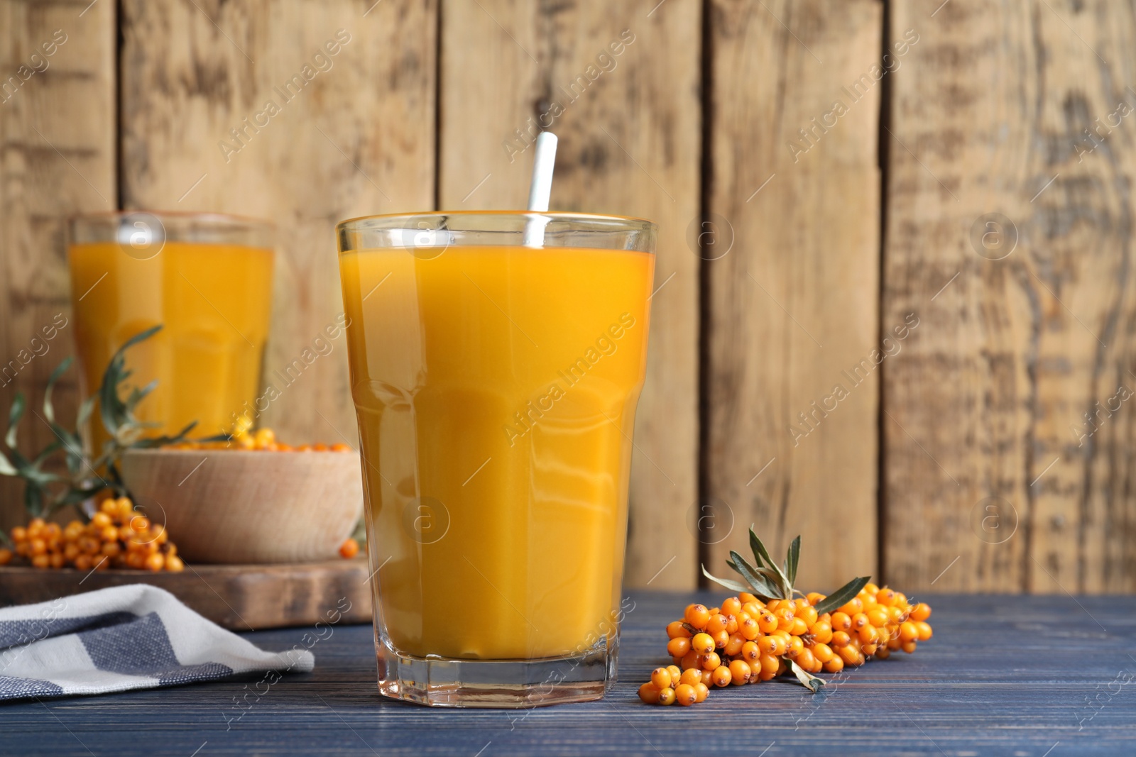 Photo of Sea buckthorn juice and fresh berries on blue wooden table, closeup