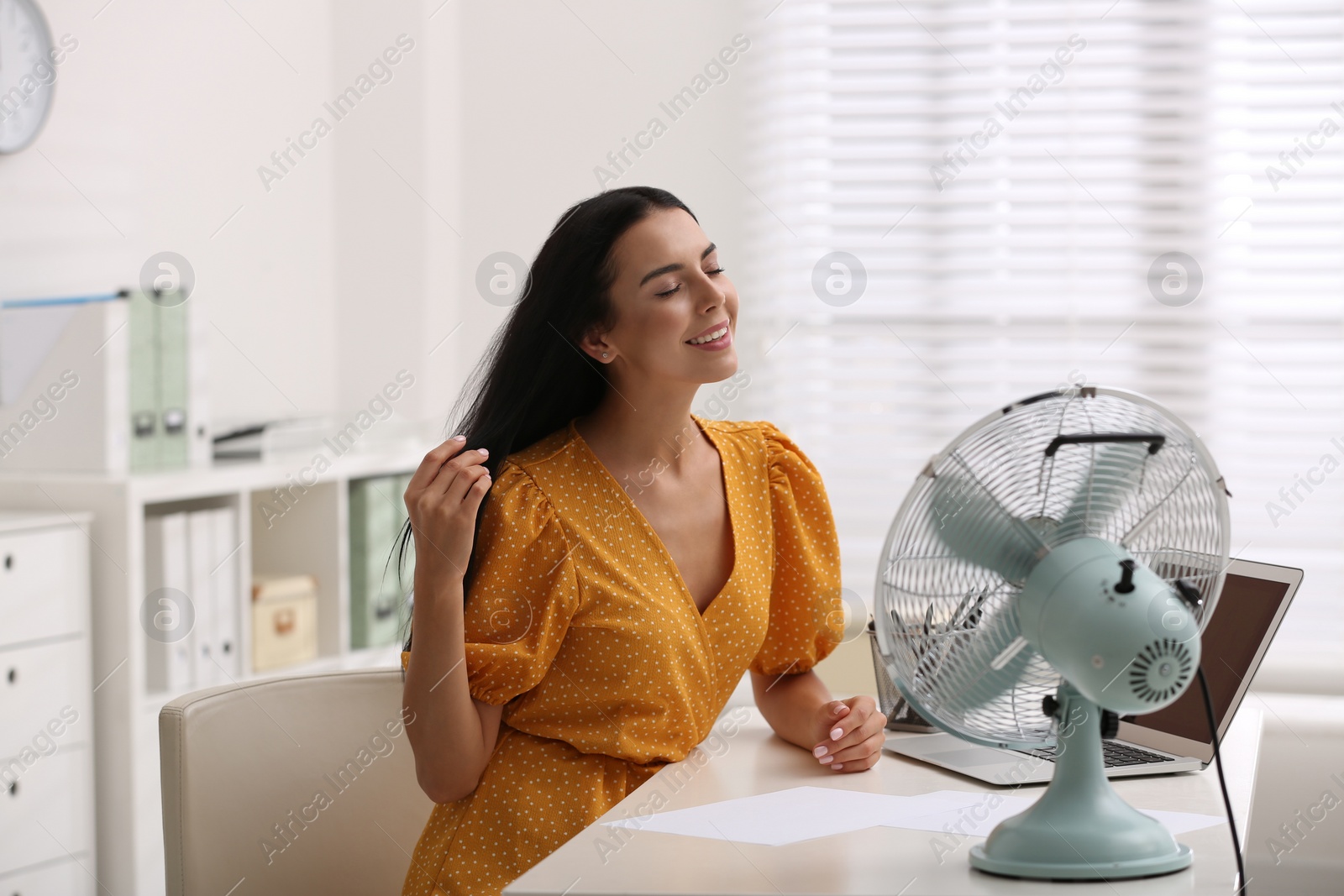 Photo of Young woman enjoying air flow from fan at workplace