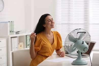 Photo of Young woman enjoying air flow from fan at workplace