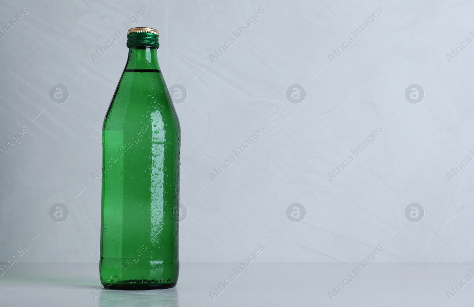 Photo of Glass bottle with water on light grey background, space for text