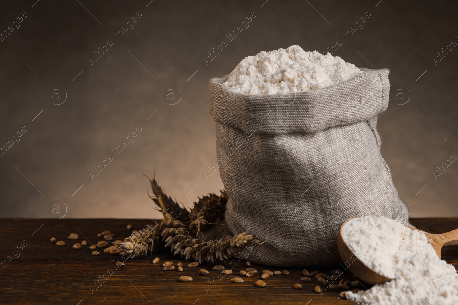 Photo of Wheat flour, grains and spikes on wooden table, space for text