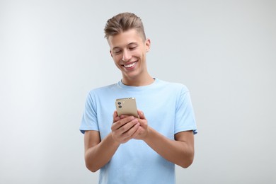 Photo of Happy young man sending message via smartphone on light grey background
