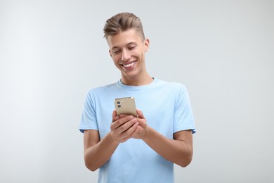 Happy young man sending message via smartphone on light grey background