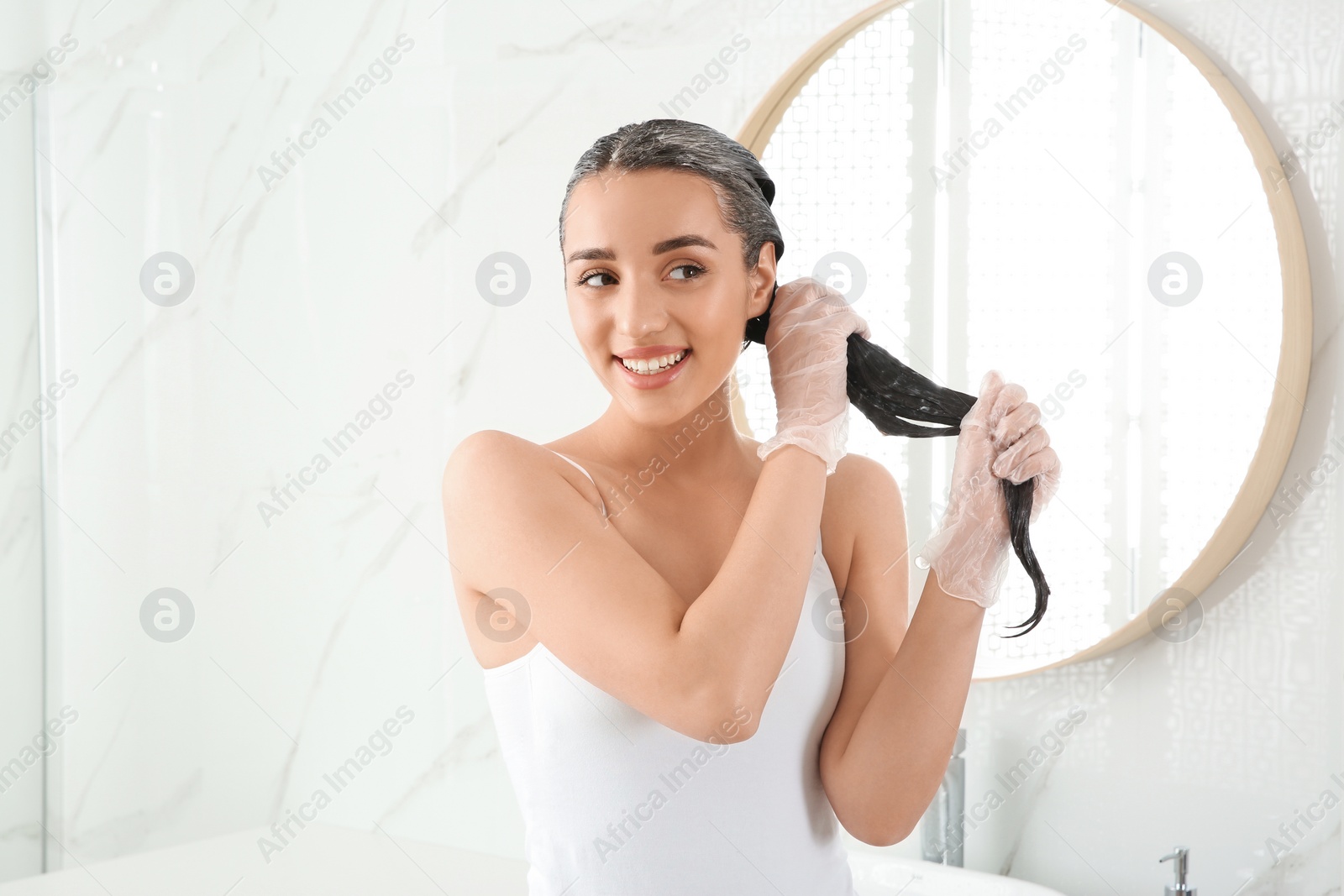 Photo of Young woman dyeing her hair in bathroom