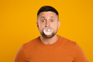 Photo of Surprised man blowing bubble gum on orange background
