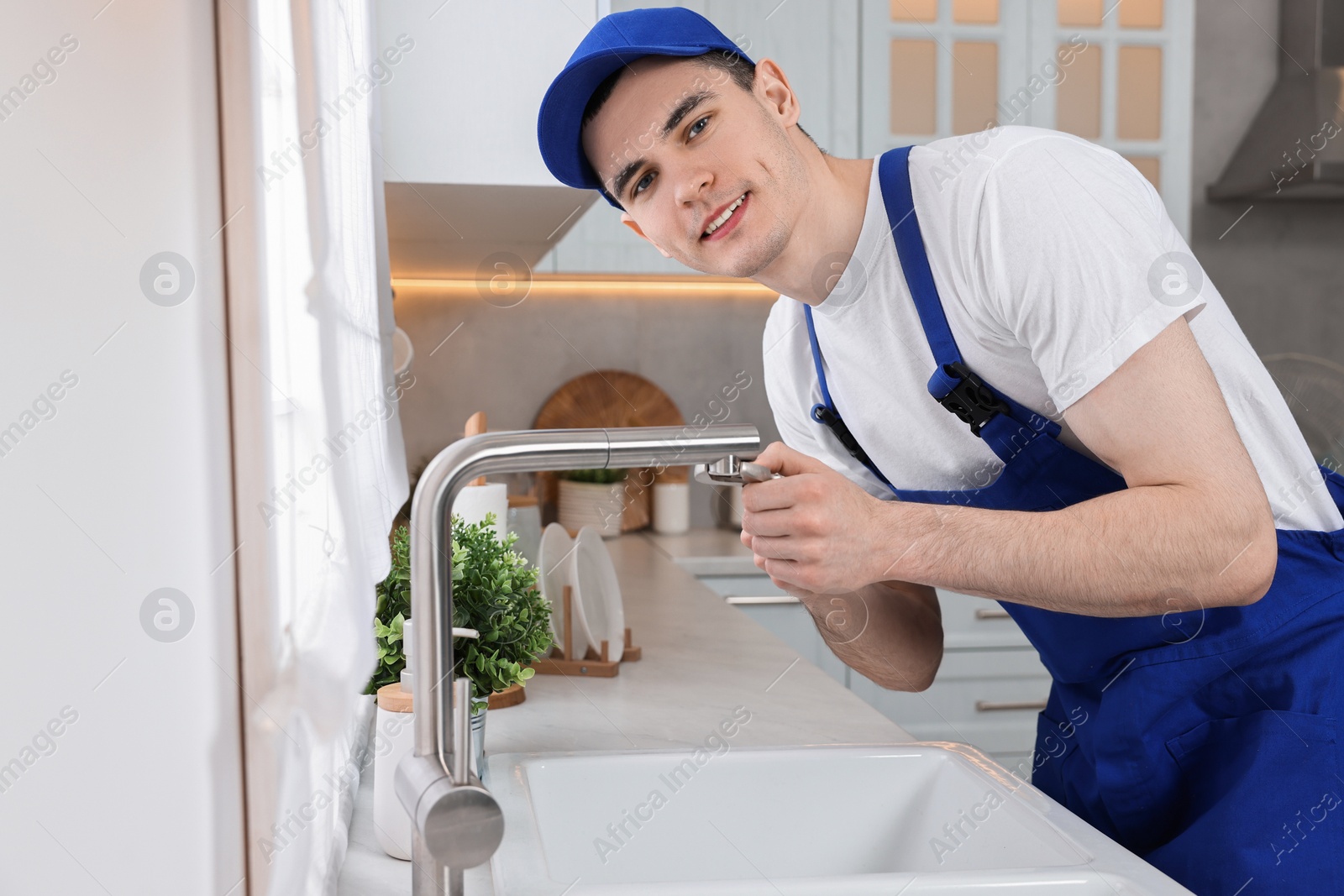 Photo of Smiling plumber repairing faucet with spanner in kitchen